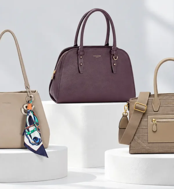Three handbags in beige, burgundy and taupe with different shapes and surface finishes in a bright studio