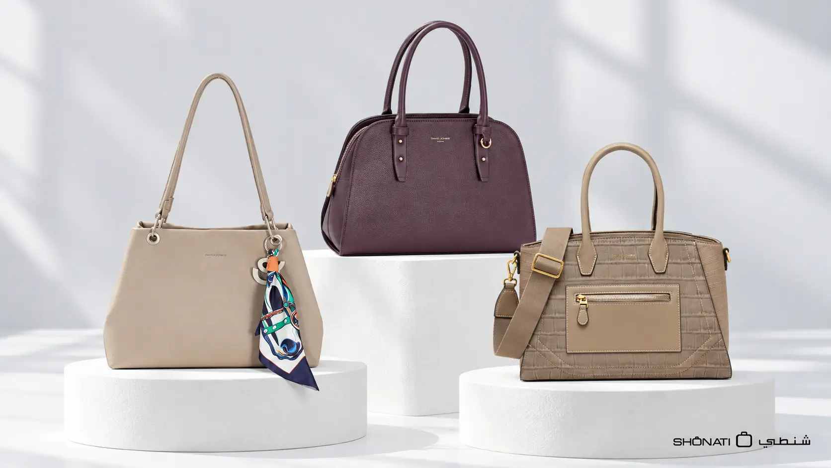 Three handbags in beige, burgundy and taupe with different shapes and surface finishes in a bright studio